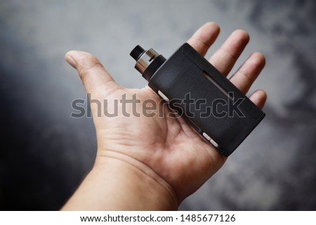 high end black regulated  box mods with rebuildable dripping atomizer in hand on dark grey texture background, vaping device, selective focus