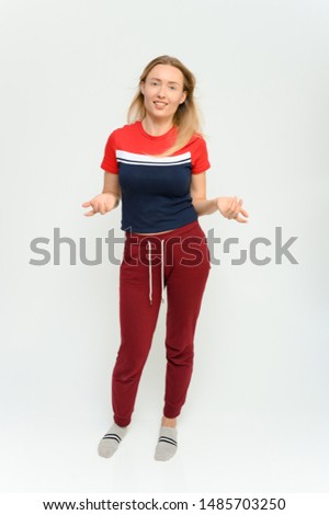 Full length studio portrait of a pretty young happy blonde woman in a tracksuit on a white background. He smiles, talks, shows with his hands, moves, shows emotions.