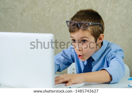 Child with glasses sitting at a laptop and watches the video. The young boy looks at the monitor in surprise.