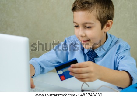 Children sitting in the office and working on a laptop. A little boy buys on the Internet. Young buyer pays by credit card.