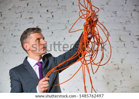 Confident mature businessman holding tangled cable against white brick wall