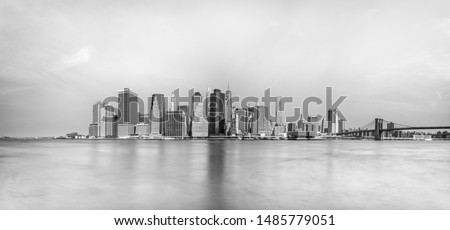 Panoramic long exposure view of lower Manhattan and Brooklyn Bridge at the water's edge in New York City.