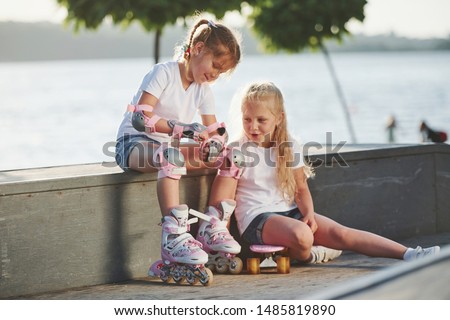 Talking with each other. On the ramp for extreme sports. Two little girls with roller skates outdoors have fun.