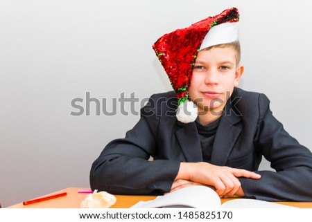 teenage boy in Santa's hat at the table with books
