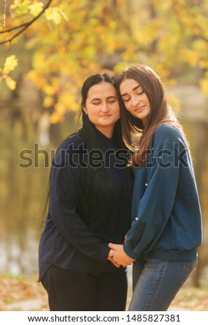 Mother with daughter stand in front of lake in the park. Yellow tree in autumn time