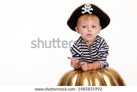 Happy child on Halloween. Funny little boy in carnival costumes of pirates standing with a big pumpkin on white background. trick or treat