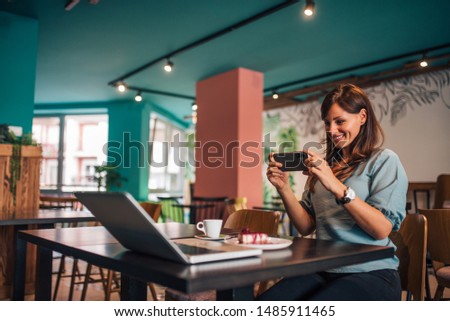 Smiling woman taking picture of dessert on smarphone at the cafe, portrait.