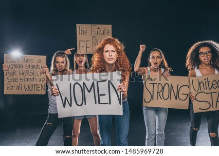 emotional multicultural women standing and holding placards on black  