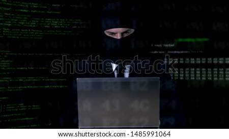 Hacker in balaclava working on laptop, illegal privacy attack, data leakage