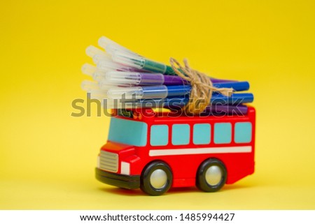 Children's toy school bus carries bright felt-tip pens. Transport on a yellow background.
