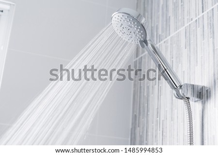 Fresh shower behind wet glass window with water drops splashing. Water running from shower head and faucet in modern bathroom. Royalty-Free Stock Photo #1485994853