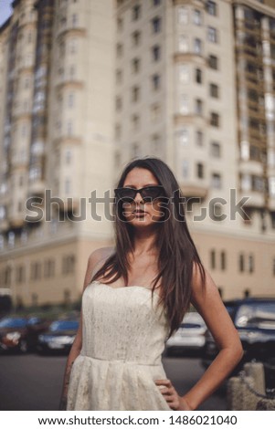 girl in a white dress with dark hair stands on the background of houses
