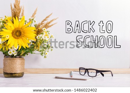The inscription marker on white board, Back to School. A table with a bouquet of flowers, glasses and attributes for writing.