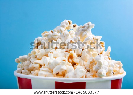 Popcorn in red and white paper cup or striped paper cup viewed from above isolated on blue background. Top view
