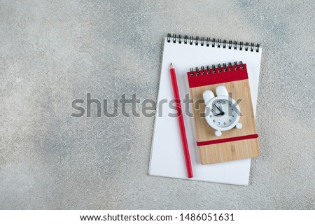 Back to school. School time minimal concept. Notepad, pencil, alarm clock on grey concrete background. Flat lay, top view