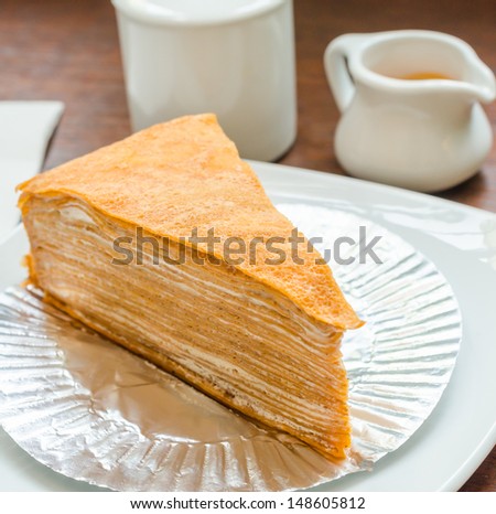 Crepe cake in white dish on the wood table with sweet sauce