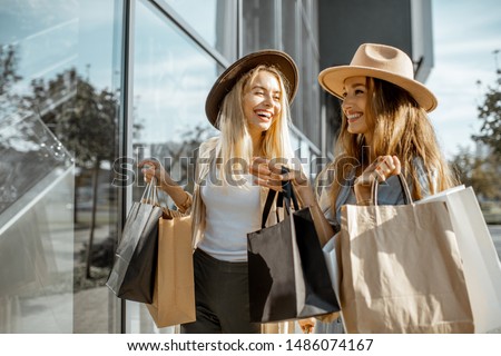 Two happy girlfriends looking on the shopwindow while standing with shopping bags near the mall Royalty-Free Stock Photo #1486074167