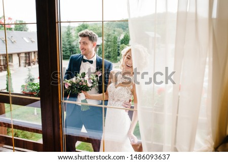 The bride and groom. Newlyweds with a wedding bouquet, standing on wedding ceremony outdoor. View through the window First meeting. Backyard.