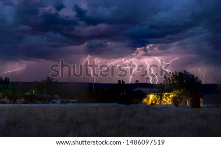 Storm lightning falling behind a house with yellow lights on and the background a black storm with blue clouds