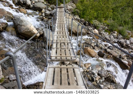 View of a small bridge over a wild stream in Folgefonna National Park, Norway. The bridge is a bit wobbly and only for hikers. Royalty-Free Stock Photo #1486103825