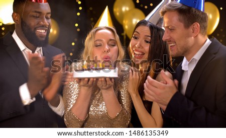 Happy blond female blowing cake candles, friends congratulating woman birthday