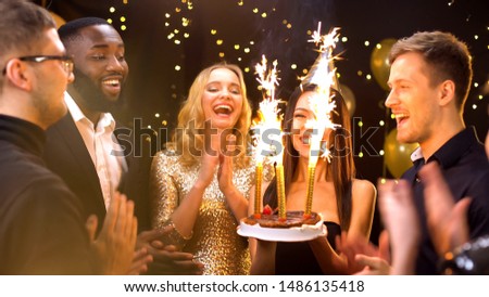 Pretty woman in party hat carrying cake with fire candles, celebrating birthday
