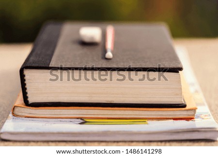 A stack of books & notebooks with pencil and eraser on a wooden desk at outdoor park. Background concept for education loan, scholarship, teachers day.
