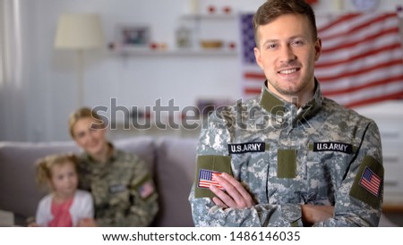 Happy male veteran of US army smiling at camera, wife and daughter on background