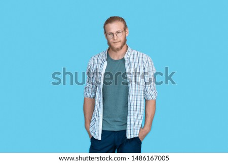Young bearded handsome man blond hair hipster wearing shirt and glasses looking at camera, millennial handsome casual guy student isolated on blue studio blank background, portrait, copy space