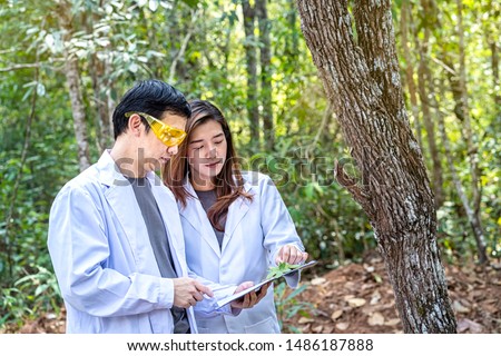 Scientists are studying plant species in the forest. Male and female scientist looking at leaf by magnifying glass in forest. Scientist ecologist in the forest take samples of plants. Royalty-Free Stock Photo #1486187888