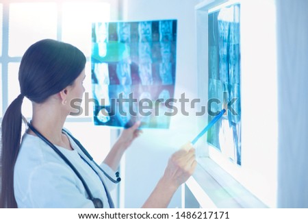 Young smiling female doctor with stethoscope pointing at X-ray at doctor's office