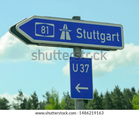 Arrow-shaped street sign pointing left to Stuttgart, Germany, the Autobahn, and U 37.