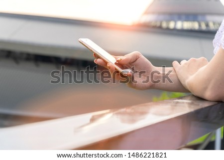 Woman typing write message on smartphone at sunset. Cropped image of young pretty girl with mobile phone. 