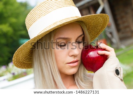 Beautiful young blonde in a straw hat holds a red apple in her hands