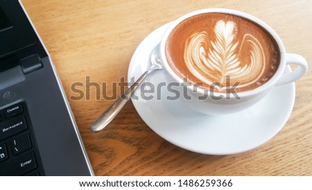a cup of Hot latte with the laptop on wood table