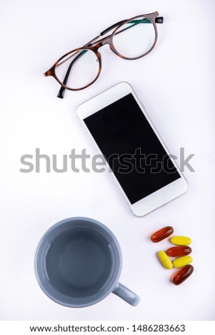 Directly above view of a close up of a cell phone cup medicine and glasses placed on a desk
