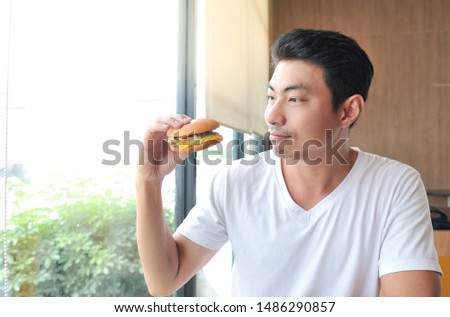 White shirt man enjoy eating with her burger in hands,A man hungry and looking his burger before eat it,selective focus