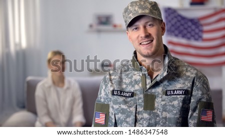 Smiling US military man looking at camera, wife sitting on background, support