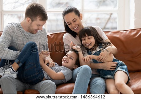 Happy funny family parents with cute little kids son daughter tickling laughing sit on sofa together, smiling couple and small children having fun playing cuddling at home enjoy funny activity