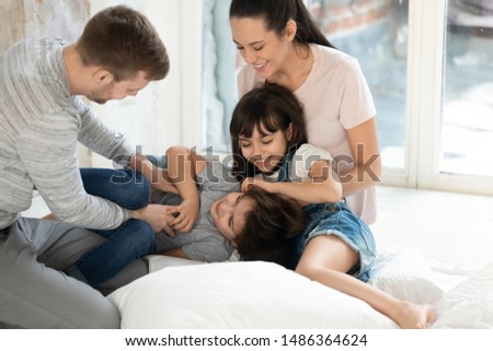 Happy family mom dad and little cute children son daughter laughing tickling on floor, parents couple having fun with small funny kids playing cuddling together at home enjoy lifestyle activity