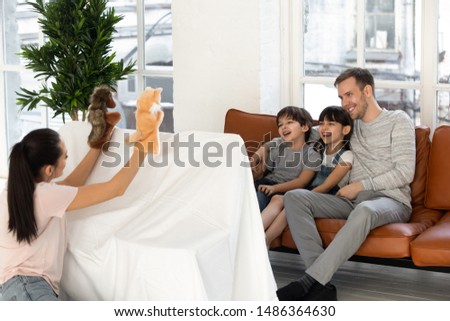 Happy father and cute kids son daughter laugh enjoy watching mom puppet show sit on sofa at home, mother play marionette toys do theatre performance for small children, creative family hobby activity Royalty-Free Stock Photo #1486364630