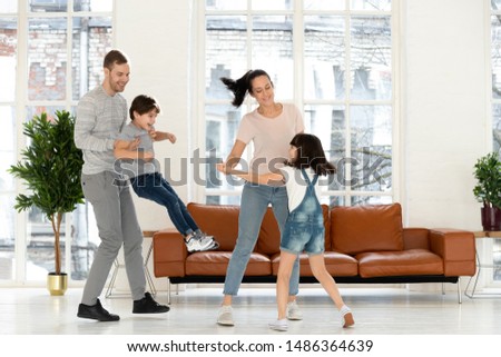 Happy active family parents couple dancing with cute small kids son daughter in modern living room interior, mom dad and little children laughing having fun together at home enjoy leisure lifestyle
