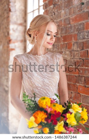 The bride stands in a loft with a bright bouquet