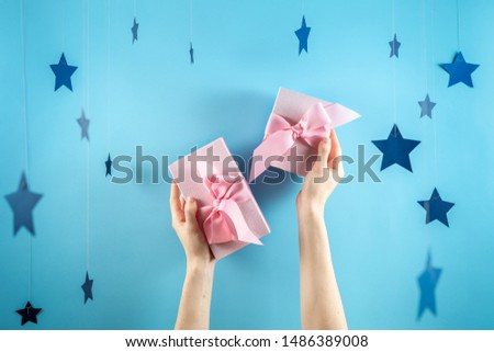 Happy birthday party! Two beautiful and pink wrapped gift box with ribbon in girls hands isolated against pastel blue background with paper stars decorations
