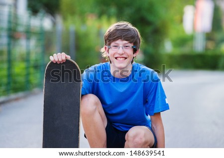 Smiling teenager crouching and holding his skateboard in a suburban setting. 