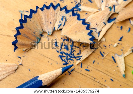 Close-up of a dark blue pencil just been sharpened with a sharpener lying next to wooden shavings on a table. The concept of creativity of children and artists