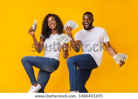 African american cheerful couple dancing with money in their hands, lifting legs up
