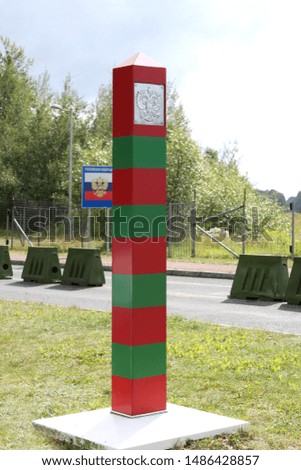 border striped pillar with the state emblem on the border between Russia and Poland, in the background a flag with an inscription in Russian of the Russian Federation