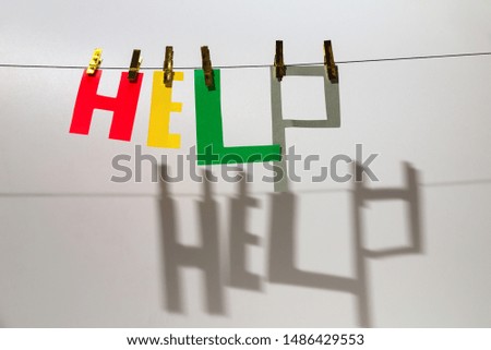 Word "Help" from different color letters is hanging at the rope on the grey background. There are shadow from the letters, clothespins. International Volunteer Day																								