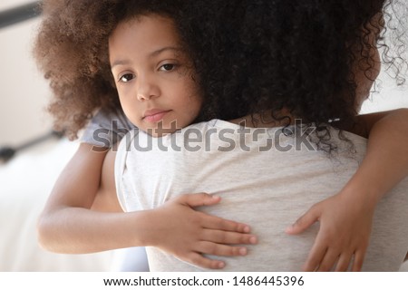 Close up head shot sad upset little cute mixed race girl hugging mom. Worried african american foster woman calming, comforting, bonding stressed unhappy adopted kid daughter. Family problem concept. Royalty-Free Stock Photo #1486445396